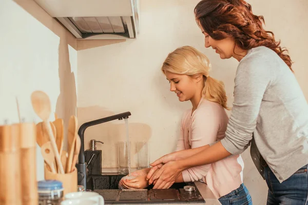 Vista lateral de mãe sorridente e criança lavando as mãos na cozinha — Fotografia de Stock