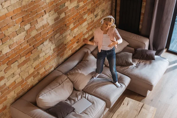 Overhead view of kid in headphones standing on couch at home — Stock Photo