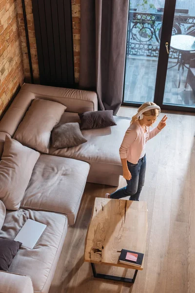 Overhead view of kid in headphones showing peace gesture near coffee table in living room — Stock Photo