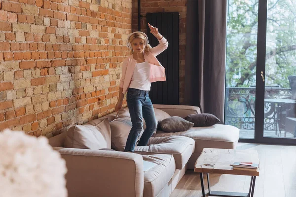 Selective focus of kid in headphones dancing on couch at home — Stock Photo