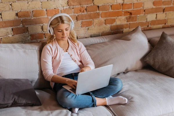 Child in headphones using laptop on couch at home — Stock Photo