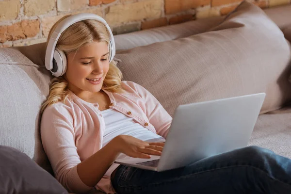 Focus selettivo del bambino sorridente in cuffia utilizzando il computer portatile sul divano in soggiorno — Foto stock