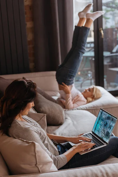 Focus selettivo della donna che utilizza il computer portatile con e salute sito web vicino figlia sul divano — Foto stock