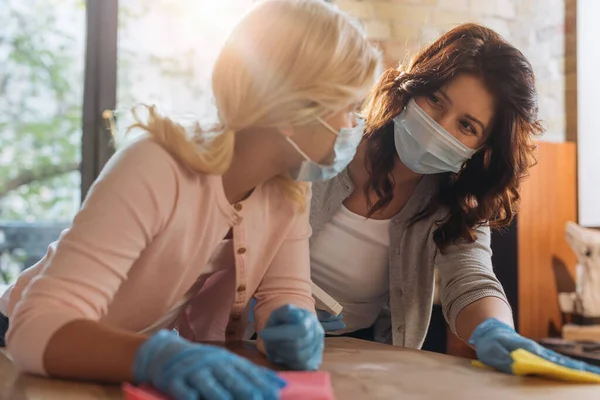 Focus selettivo di bambino e madre in maschere mediche pulizia tavolino da caffè a casa — Foto stock