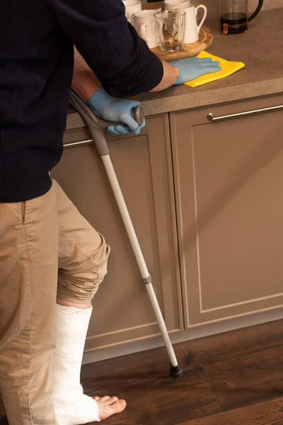 Ausgeschnittene Ansicht eines Mannes mit Gipsverband an der Arbeitsplatte zur Beinreinigung in der Küche — Stockfoto