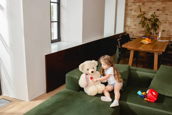 Lindo niño sosteniendo estetoscopio de juguete cerca de oso de peluche mientras juega médico juego - foto de stock