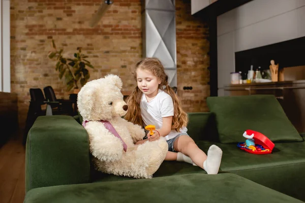 Lindo niño sosteniendo juguete cerca de oso de peluche mientras juega médico juego - foto de stock