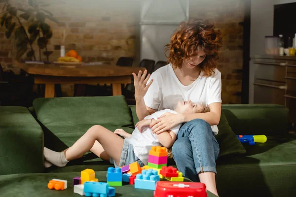 Curly mother looking at cute daughter near building blocks — Stock Photo