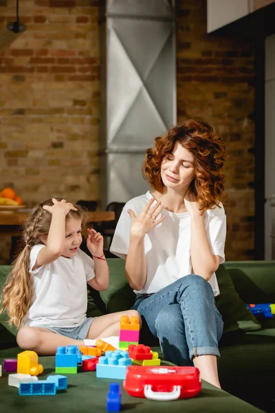 Redhead mother looking at adorable daughter near building blocks — Stock Photo