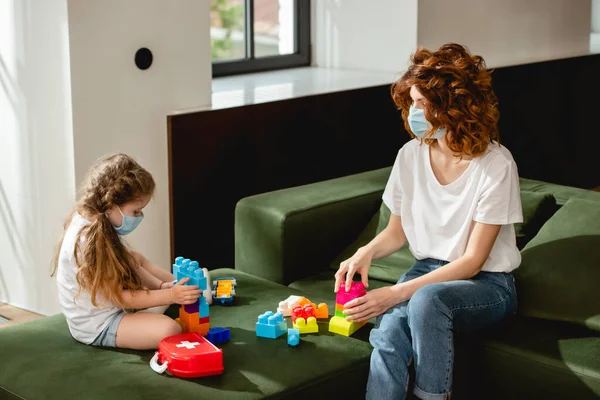 Redhead mother and daughter in medical masks playing building blocks — Stock Photo