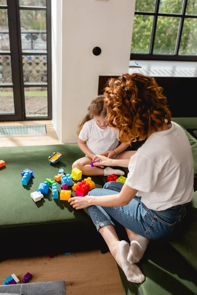 Vue arrière de la mère rousse et fille mignonne jouant blocs de construction dans le salon — Photo de stock