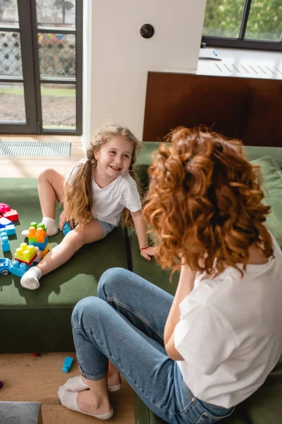 Selective focus of cheerful kid looking at redhead mother near building blocks on sofa — Stock Photo
