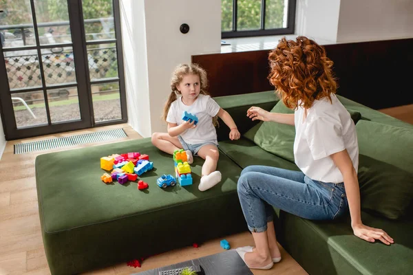 Back view of redhead mother looking at upset daughter and building blocks — Stock Photo