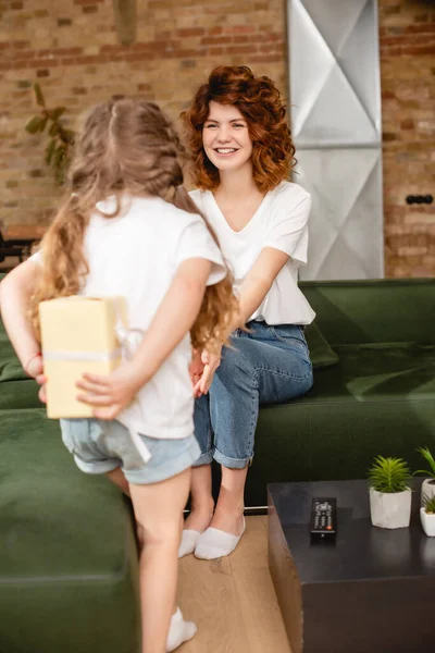 Back view of cute kid hiding present behind back near curly mother — Stock Photo