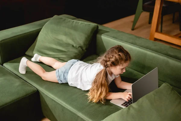 Niedliches Kind auf Sofa liegend und mit Laptop — Stockfoto