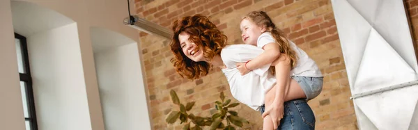 Tiro panorâmico de encaracolado mãe piggybacking bonito filha — Fotografia de Stock