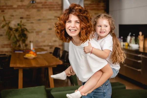 Alegre e encaracolado mãe piggybacking bonito filha — Fotografia de Stock