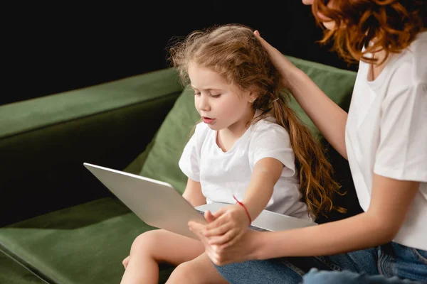 Selektiver Fokus der rothaarigen Mutter mit Laptop und anrührenden Haaren der Tochter im Wohnzimmer — Stockfoto