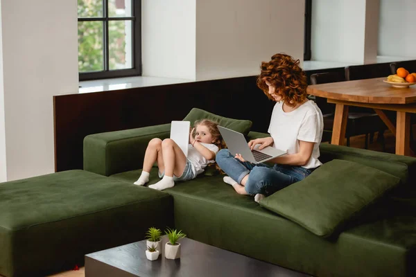 Redhead freelancer using laptop near cute daughter with digital tablet — Stock Photo