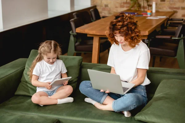 Redhead freelancer using laptop near daughter with digital tablet — Stock Photo