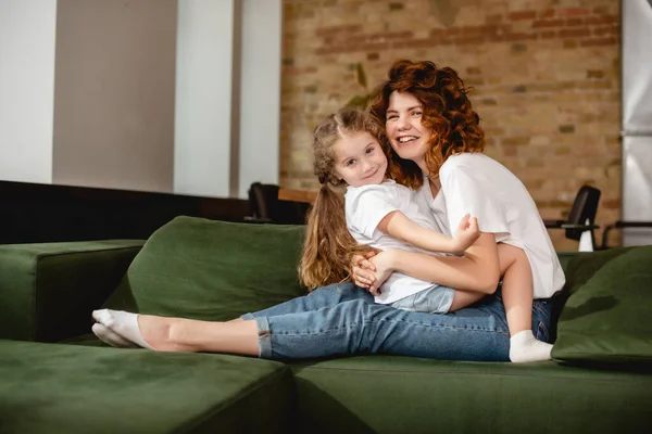 Happy daughter hugging cheerful and curly mother — Stock Photo