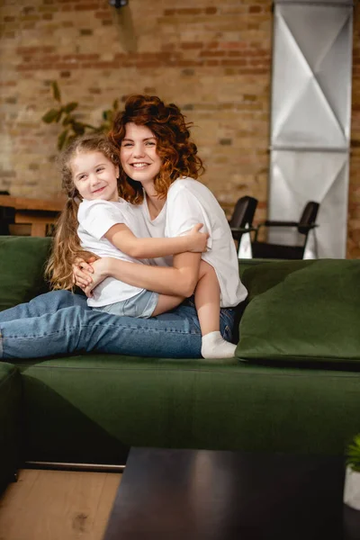 Cute daughter hugging cheerful and curly mother — Stock Photo