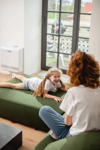 Selective focus of kid lying on sofa and looking at curly mother — Stock Photo