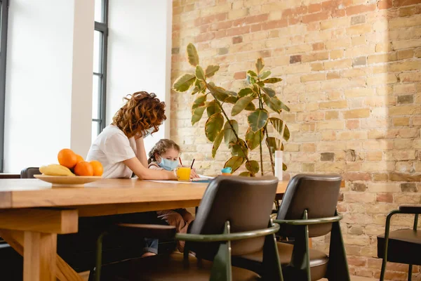 Selective focus of mother in medical mask near daughter and fruits at home — Stock Photo