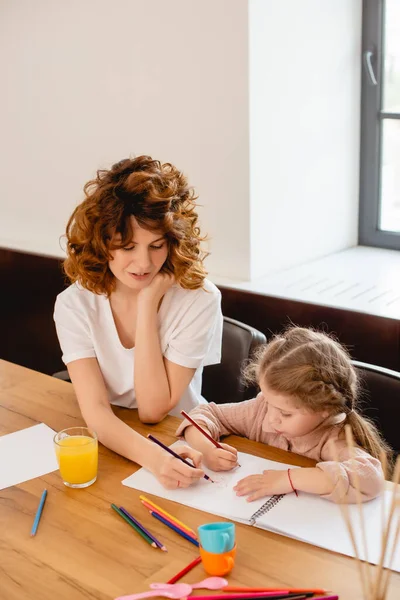 Кучерява мати малює з милою дочкою вдома — Stock Photo