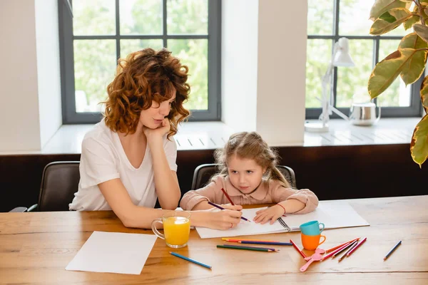 Rizado madre dibujo con adorable hija en casa - foto de stock