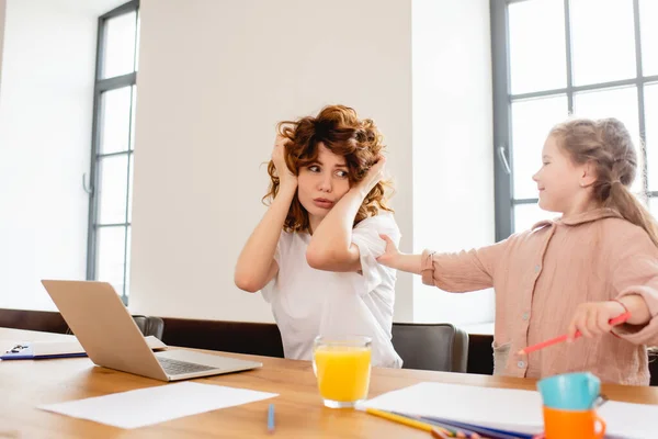 Fille touchant mère bouclée couvrant oreilles près d'un ordinateur portable — Photo de stock