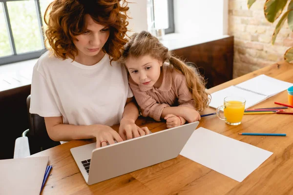 Lindo niño mirando portátil mientras freelancer madre trabajando desde casa - foto de stock