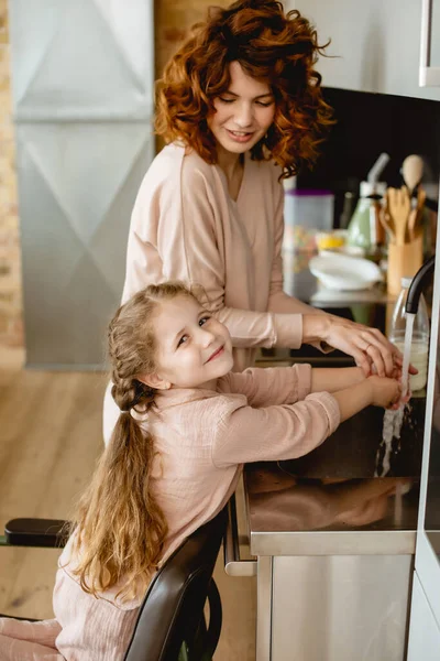 Curly mother and happy daughter washing hands — Stock Photo