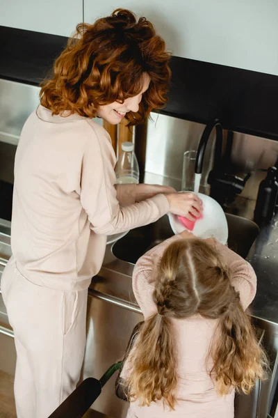 Back view of kid washing plate with happy mother — Stock Photo