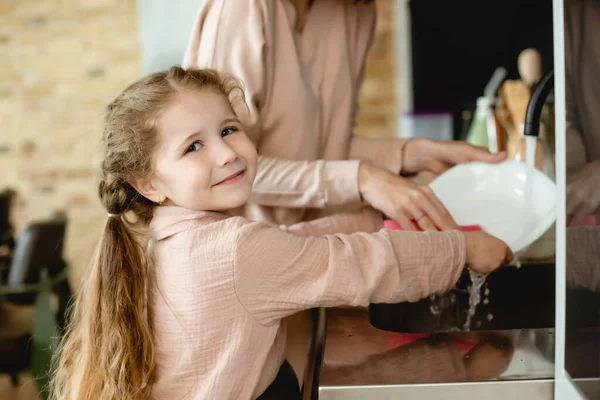 Избирательный фокус счастливого ребенка мыть тарелку с матерью — стоковое фото