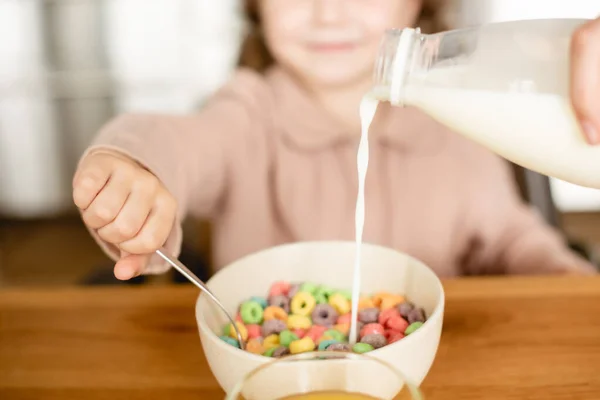 Foyer sélectif de lait versant dans le bol avec de savoureux flocons de maïs près de mignon enfant — Photo de stock