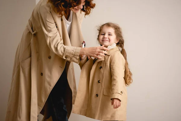 Mãe feliz tocando casaco de trincheira na criança alegre — Fotografia de Stock