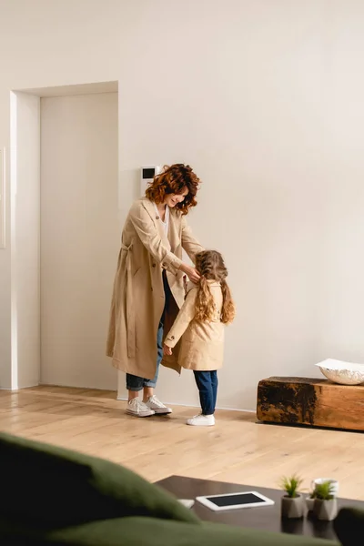 Selective focus of happy mother looking at daughter in trench coat — Stock Photo