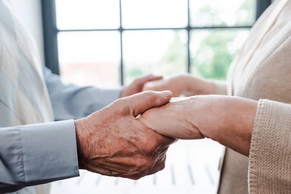 Vista recortada de pareja de ancianos tomados de la mano en casa - foto de stock