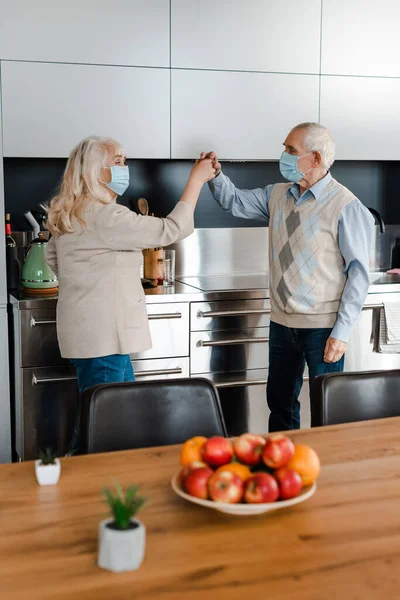 Elderly couple in medical masks dancing at home during self isolation — Stock Photo
