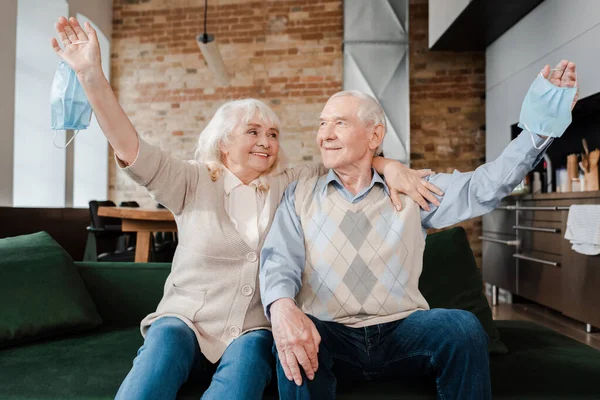 Glückliches älteres Paar mit medizinischen Masken auf dem Sofa nach der Quarantäne — Stockfoto