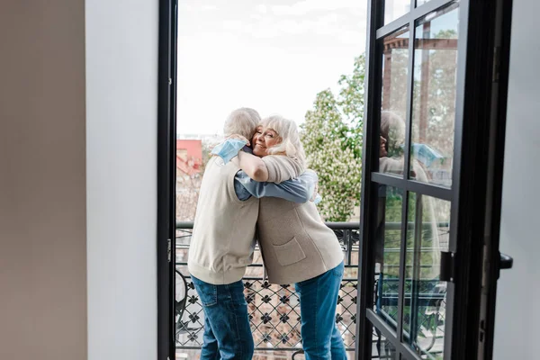 Heureux couple âgé tenant masques médicaux et câlins sur le balcon après auto isolement — Photo de stock