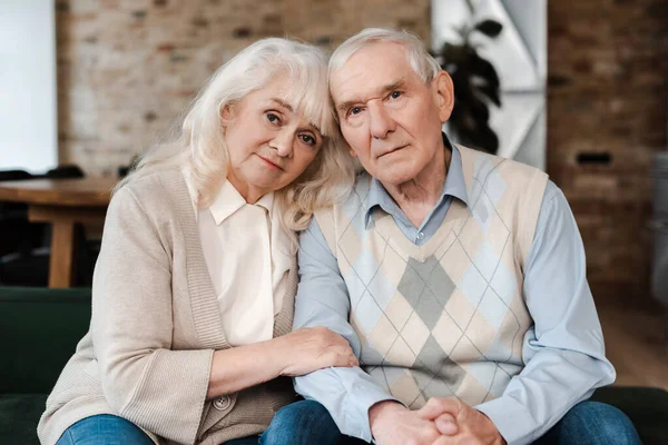 Pareja de ancianos abrazándose y sentados en casa en cuarentena - foto de stock