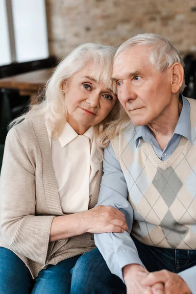 Triste anciano esposa y marido abrazando y sentado en casa en cuarentena - foto de stock