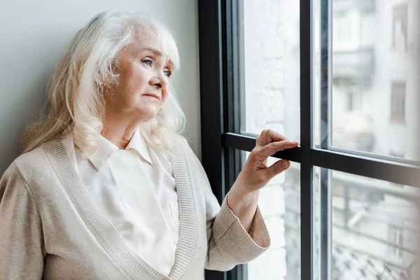 Triste anciana mirando por la ventana durante el auto aislamiento - foto de stock