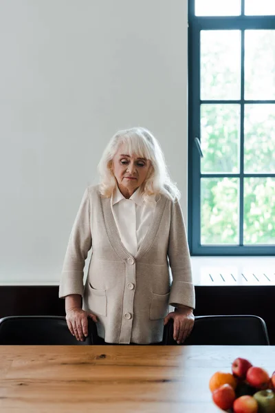 Upset lonely elderly woman standing at table with fruits during quarantine — Stock Photo