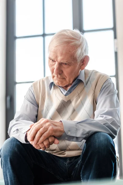 Расстроен старший мужчина сидит один на диване во время самоизоляции — стоковое фото