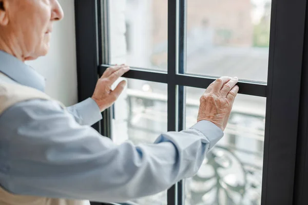 Abgeschnittene Ansicht eines älteren einsamen Mannes, der durch ein Fenster auf Selbstisolierung blickt — Stockfoto