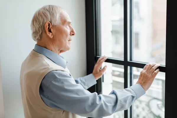 Sad elderly man looking through window during quarantine — Stock Photo