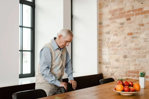 Chateado homem idoso em pé à mesa com frutas durante a quarentena — Fotografia de Stock